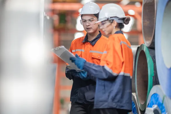 Operarios revisando documentación técnica sobre ensayos no destructivos en una fábrica de tubos metálicos.