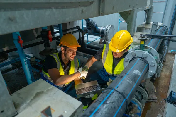 Técnicos con laptop cierran un acuerdo de servicios de mantenimiento industrial en la zona de bombeo de una empresa.