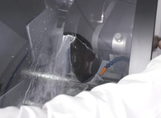 Proceso de corte húmedo con chorro de refrigerante sobre muestra metálica para análisis metalográfico.