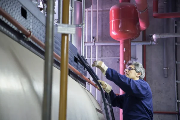 Técnico con guantes y traje azul inspecciona una caldera industrial antes de realizar un ensayo con corrientes inducidas.
